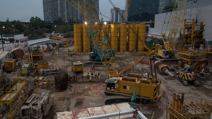 Builders and lifting cranes working on construction site in late evening. Hong Kong