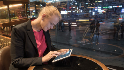 Young woman using tablet computer in the cafe in the evening, people and traffic in the street outside. Seoul, South Korea