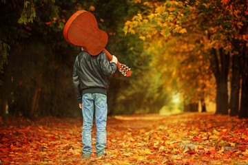 Boy with guitar walking on the autumn road. Back view