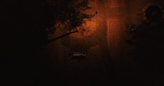 Camera goes down in mystery light near mysterious man who's sitting in the park. Aerial night drone footage.  Good start for a Halloween background. Looks like thriller