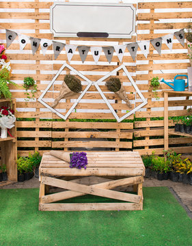 photo booth for congraturation made from wooden wall with empty sign decorated by small plants and bouquets