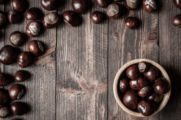Pile of horse chestnuts on a bamboo bowl on wooden table - vintage