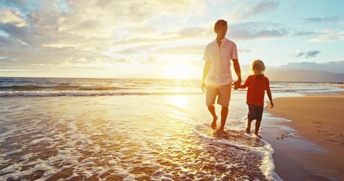 Father and son walking on the beach at sunset