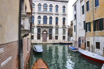 Narrow canal among old colorful brick houses and boats in Venice, Italy.