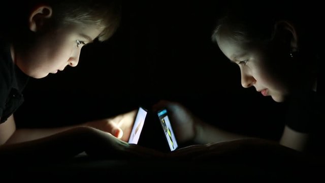 children look to smartphones in the dark on black background