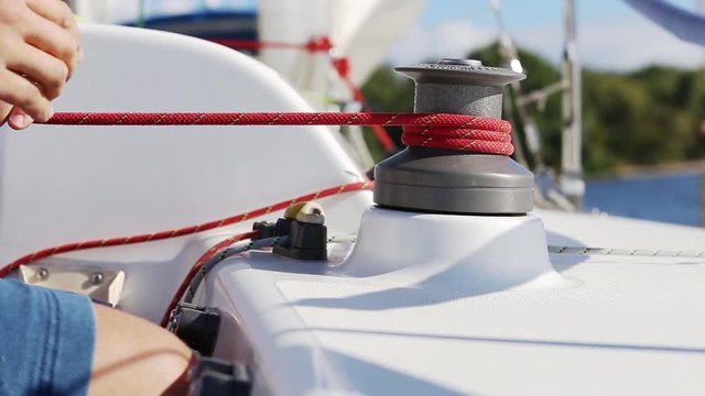 Sailing crew member on sailboat trimming front sail by winch