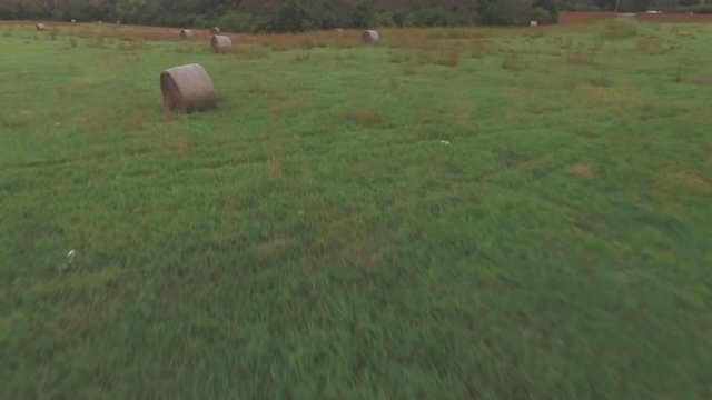 Aerial fly over of bails of hay in field.