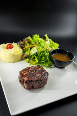 Plate with thick juicy stake, bowl of red sauce, golden french fries and green vegetables. Studio shot with black wooden background.