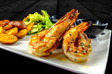 Haute cuisine plate with shrimps, beef steak, fried potatoes, salad and two bowls of sauce. Shot in studio with balck wood background.
