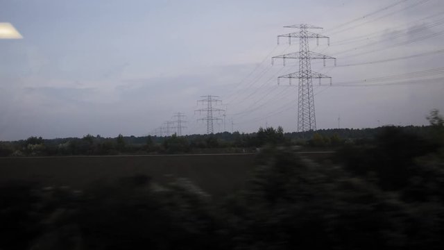 View from train - High voltage tower, meadows, wind energy turbine