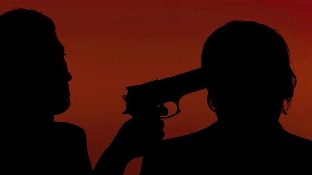 A woman pointing a handgun to a man's temple. Crime, violence, robbery. Silhouette shot.
