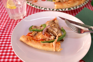 Slice of vegetarian pizza with cheese, tomato sauce, green peppers, mushrooms and onion in a pizzeria. Selective focus. 