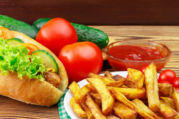Fototapeta na wymiar Fast food meal, hot dog, french fries, ketchup, tomato and cucumber on wooden background.