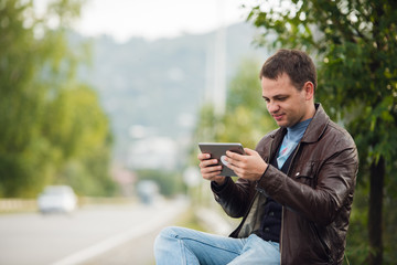 Man sitting on a road fence with gps tablet pc and using online maps