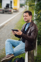 Fototapeta premium Man orders taxi from his tablet sitting on a road fence
