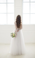 Bride standing at a window back with bouquet.