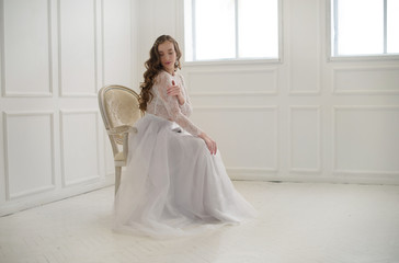 Beautiful young bride sitting on a chair in white room.