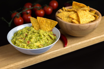 Guacamole in white bowl on natural wooden desk.