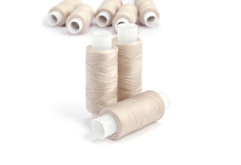 Spools of beige cotton threads on white background 