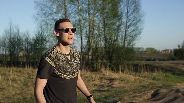 Stylish young man in sunglasses catches a flying disc in nature