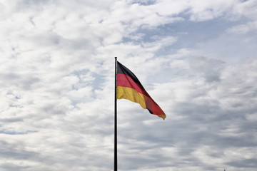 German flag waves with cloudy sky background in front of Reichstag building in Berlin.