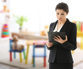 Female teacher with clipboard on blurred playroom background