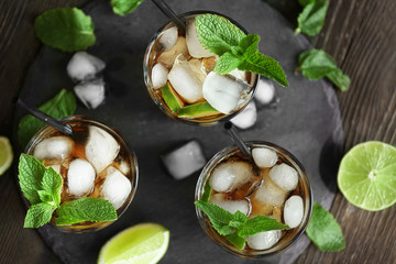 Glasses of cocktail with ice and mint on wooden table, top view