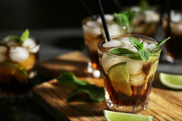 Glass of cocktail with ice on wooden cutting board closeup