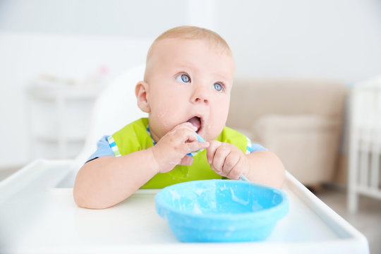 Little baby eating from bowl with spoon indoors