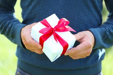man's hand with a small white gift box with bow