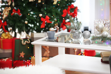 Cup and glass vases with Christmas decor on white table in living room decorated for Christmas