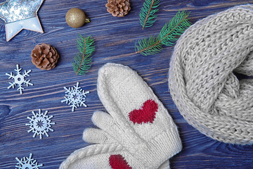 Knitted scarf, mittens and Christmas decor on wooden background