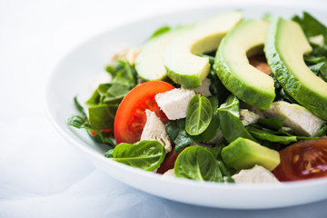 Fresh salad with chicken, tomatoes, spinach and avocado on white background close up. Healthy food.