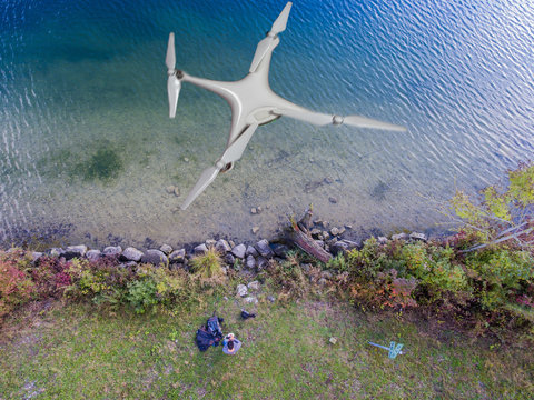 Luftbild See - Mann am Ufer lenkt Flugdrohne mit Fernsteuerung