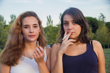 Two girls friends smoking cigarettes in the park on a cloudy day. They are of celebration and are happy. 