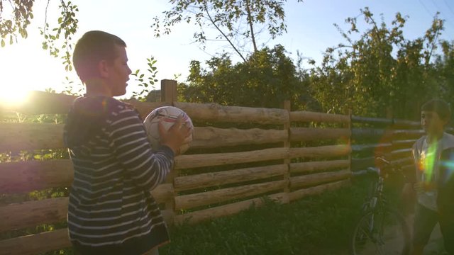 Two boys playing ball outdoors at sunset, throw ball with hands in farm