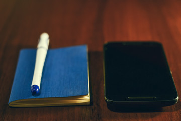 Pocket book, pen and mobile smart phone on wooden table