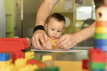 Little child and father are drawing on a paper.