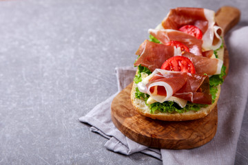 Sandwich with ciabatta, prosciutto,brie cheese and lettuce.on the Board, a grey stone background.