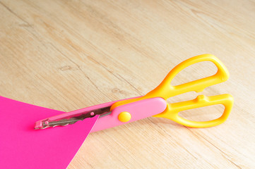 A colorful scissor that cut a zigzag pattern with a pink paper 