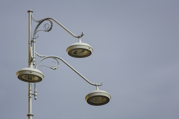 Closeup of retro stylish street lamppost with three bulbs over grey cloudy sky. Copy space.