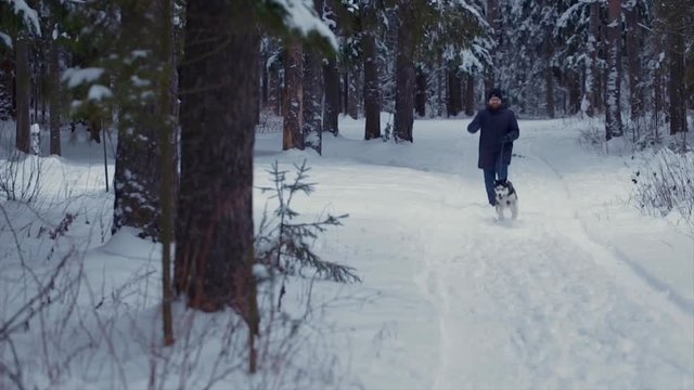 Man runs with the dog Husky in a winter forest towards the camera