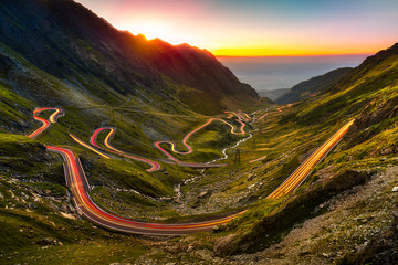 Traffic trails on Transfagarasan pass at sunset. Crossing Carpathian mountains in Romania, Transfagarasan is one of the most spectacular mountain roads in the world. - obrazy, fototapety, plakaty