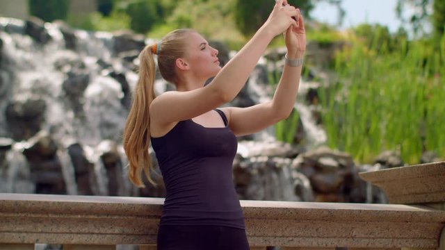 Selfie girl. Caucasian girl taking selfie near waterfall. Selfie woman. Woman selfie. Young woman taking self photo in park. Different expressions on woman face. Sport woman making self portrait