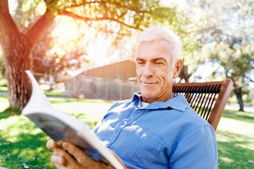 Senior man sittingin park while reading book