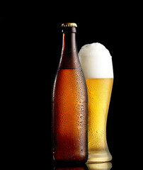 Bottle and glass of beer on the wooden table over black background
