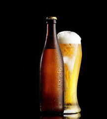 Bottle and glass of beer on the wooden table over black background