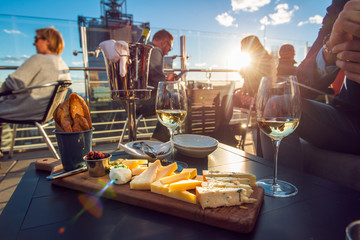 People having dinner at rooftop restaurant with wine and cheese at sunset time. - 124689367