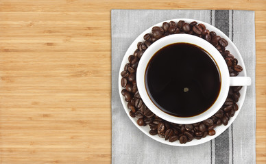 top view dark coffee with beans in white cup on plate mat and wo