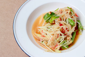 Green Papaya Salad (Som tum Thai) in white dish on wood table, Thai cuisine spicy delicious